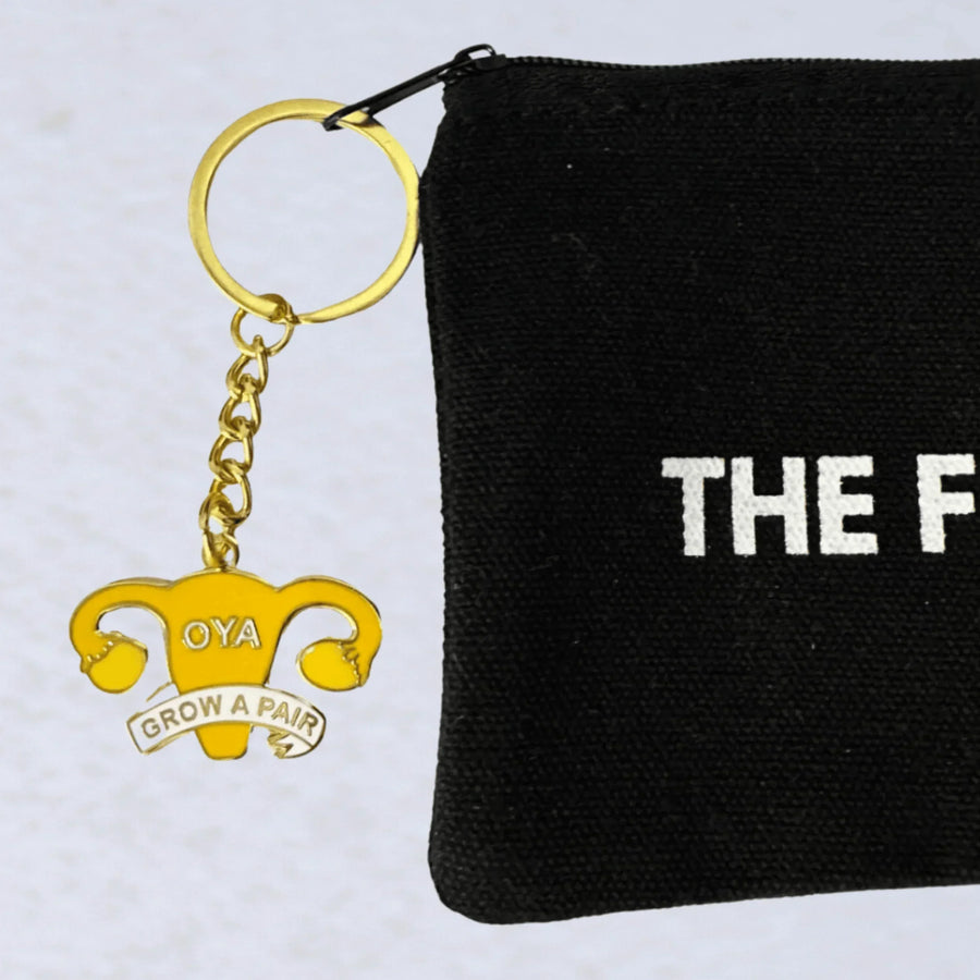 Oya Femtech keychain shaped like a uterus with text Grow a Pair, attached to black pouch with white text