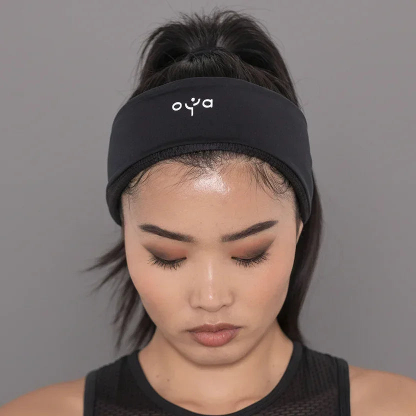Close-up of a woman wearing a black Oya Femtech headband and black activewear against a gray background