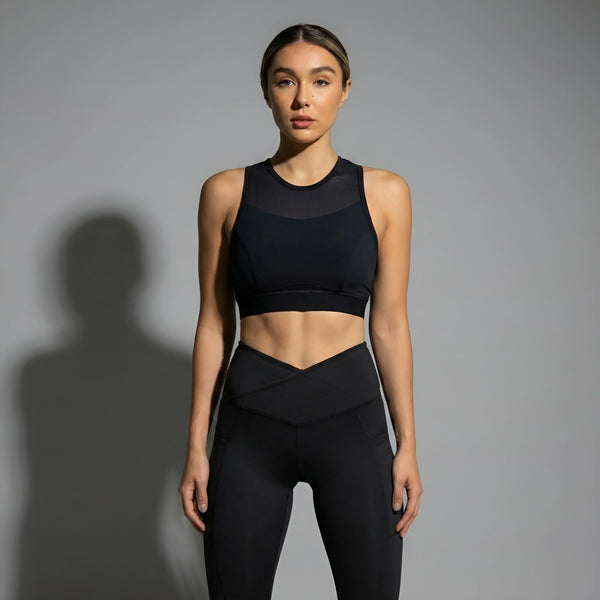 Woman wearing black high-waisted leggings and a matching black sports bra activewear set against gray background