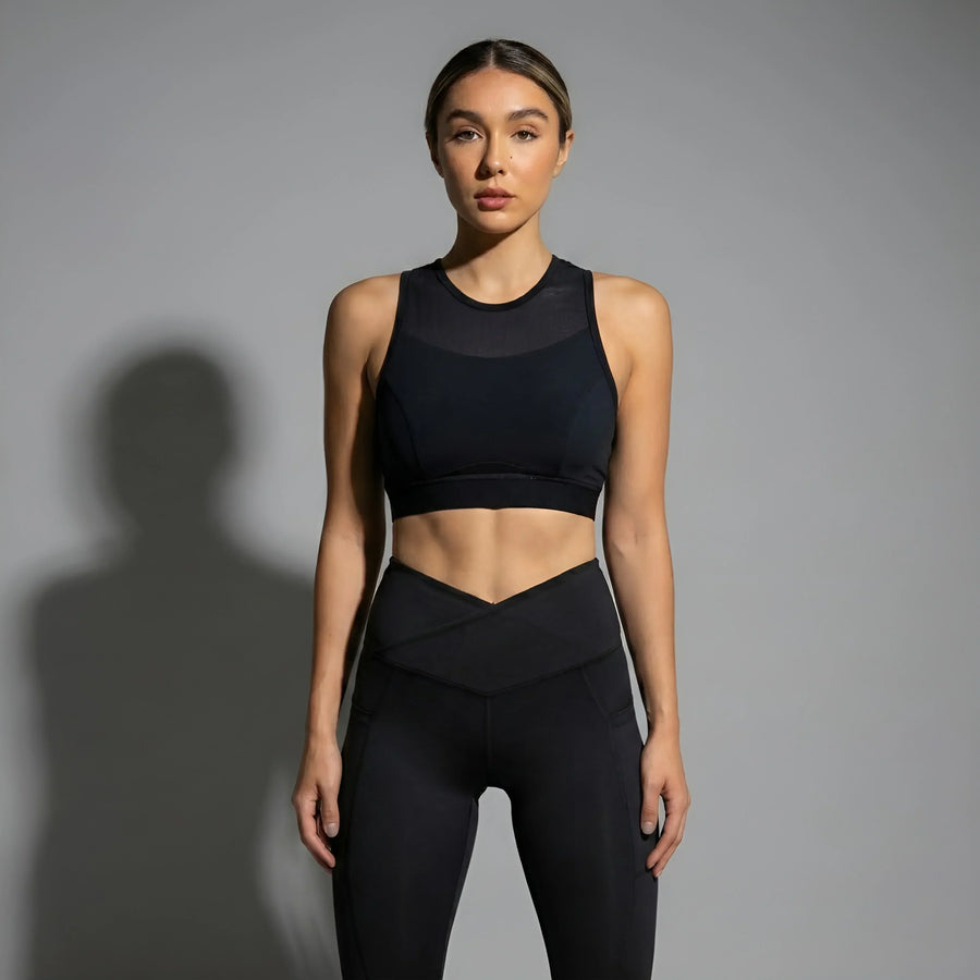 Woman wearing black high-waisted leggings and a matching black sports bra activewear set against gray background
