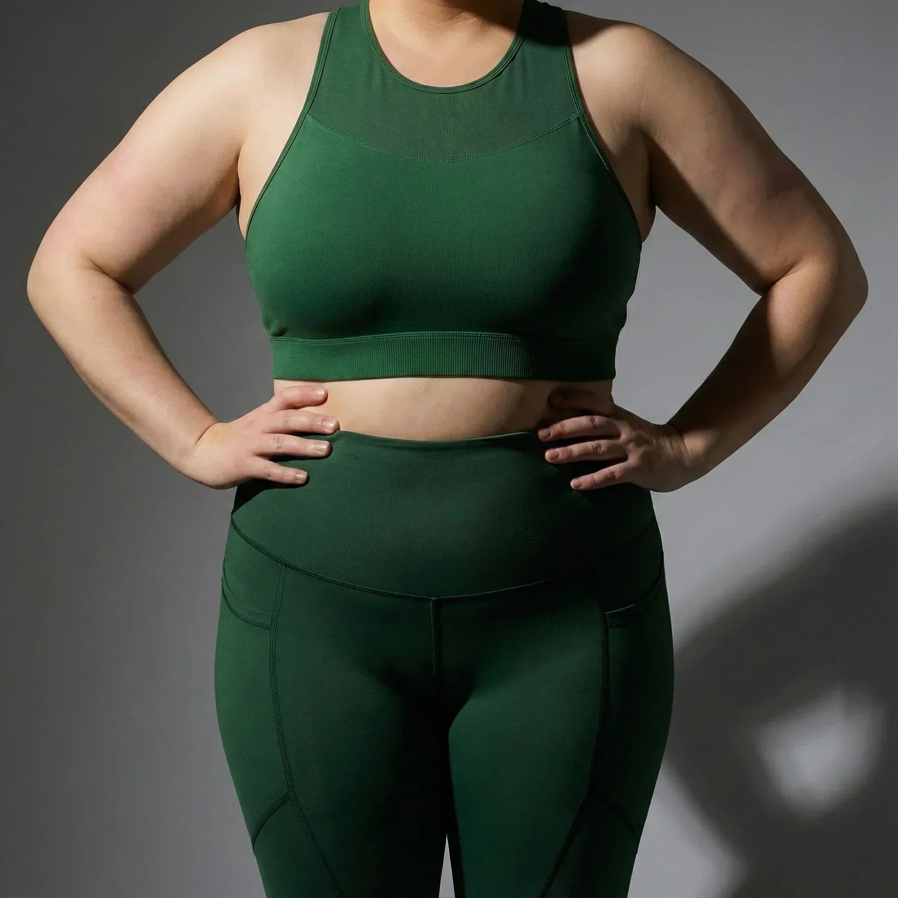 Plus size woman wearing green femtech activewear set with sports bra and high-waisted leggings