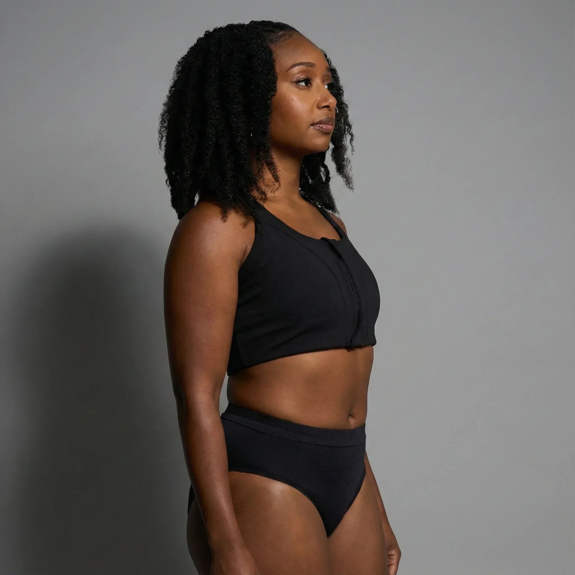 Woman wearing black Oya Femtech activewear with cooling and moisture control, standing against gray background