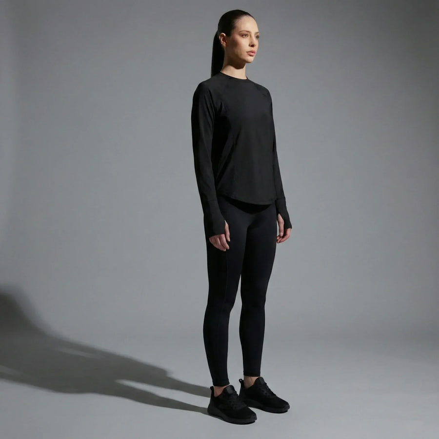 Woman wearing black long-sleeve activewear top and leggings, standing in minimalist gray studio