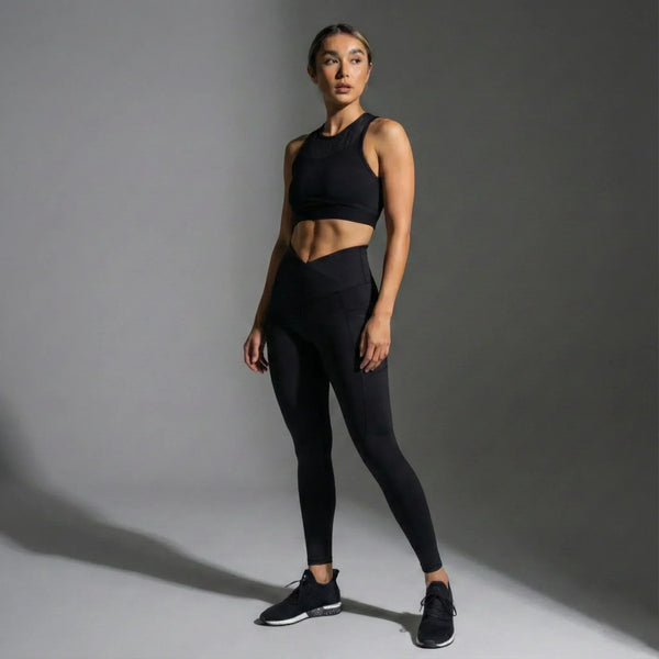 Woman wearing black high-waist leggings and black sports bra in studio, showcasing femtech activewear