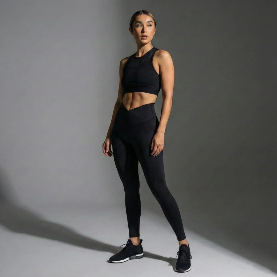 Woman wearing black high-waist leggings and black sports bra in studio, showcasing femtech activewear
