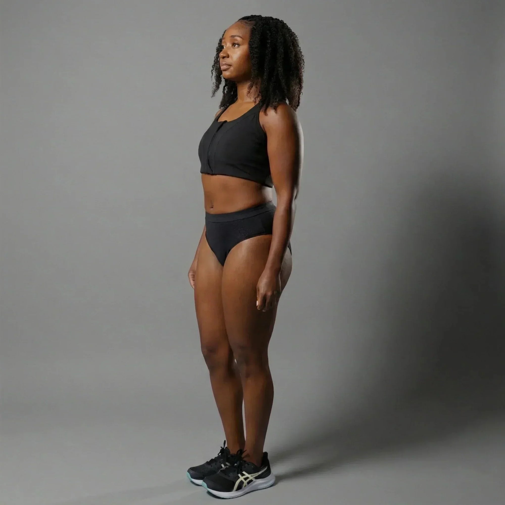 Woman wearing black Oya Femtech cooling activewear set with sports bra and briefs, standing on gray background