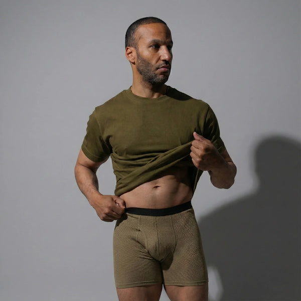 Man lifting olive green shirt showing olive green boxer briefs with black waistband on gray background