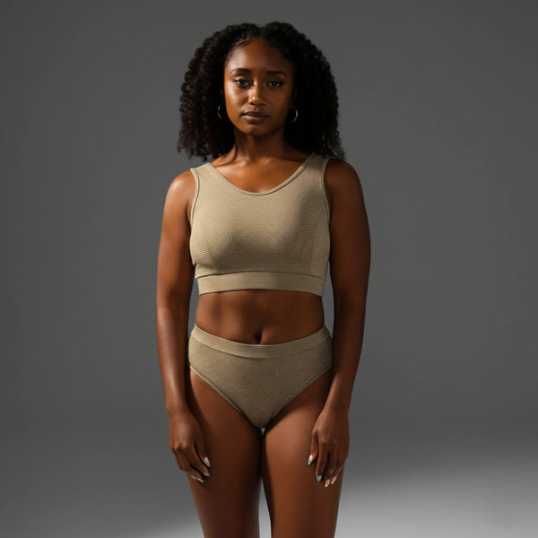Woman wearing beige ribbed femtech activewear set with crop top and high-waist briefs on gray background