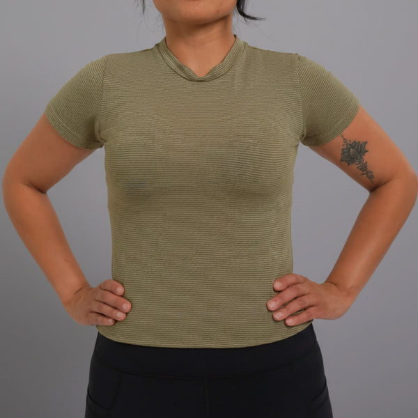 Woman wearing olive green ribbed short-sleeve femtech activewear top and black pants, hands on hips