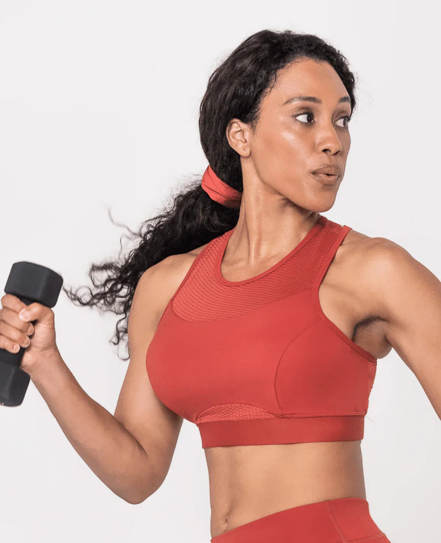 Woman in red activewear with matching scrunchie doing dumbbell workout, showcasing Oya Femtech Apparel